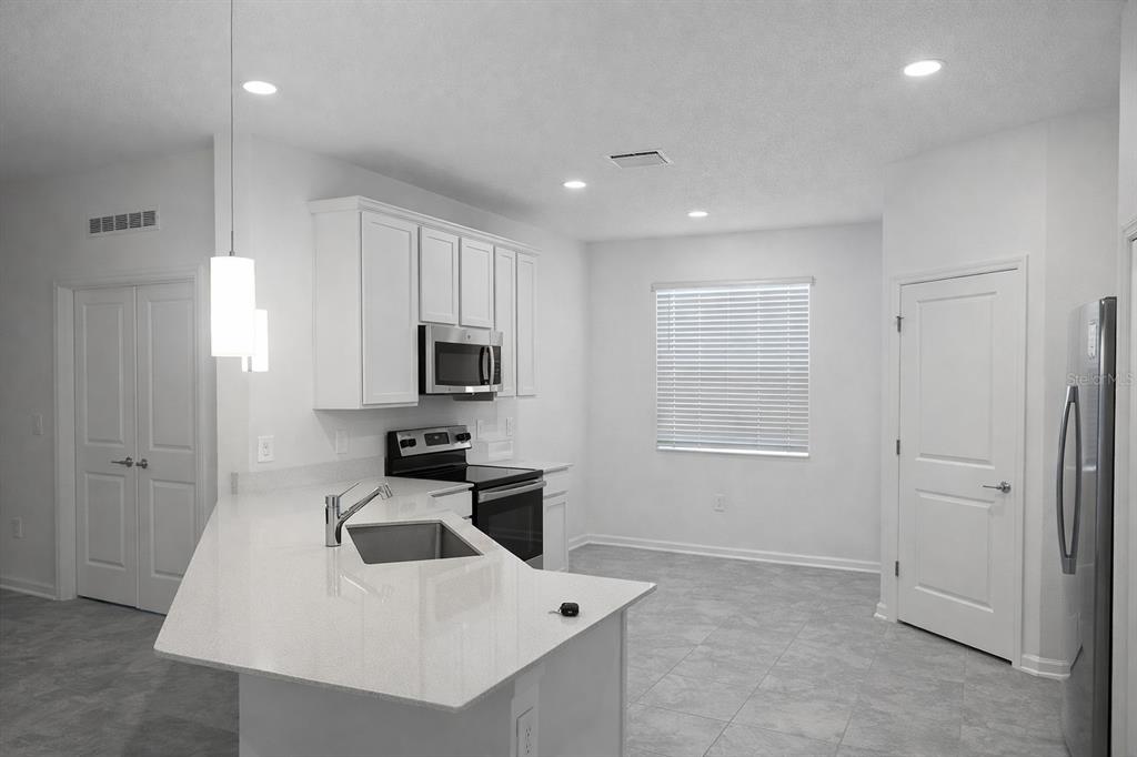 A modern kitchen features white cabinets, quartz countertops, stainless steel appliances, and tile flooring — 4086 GOOSEBERRY TRAIL, KISSIMMEE, FL