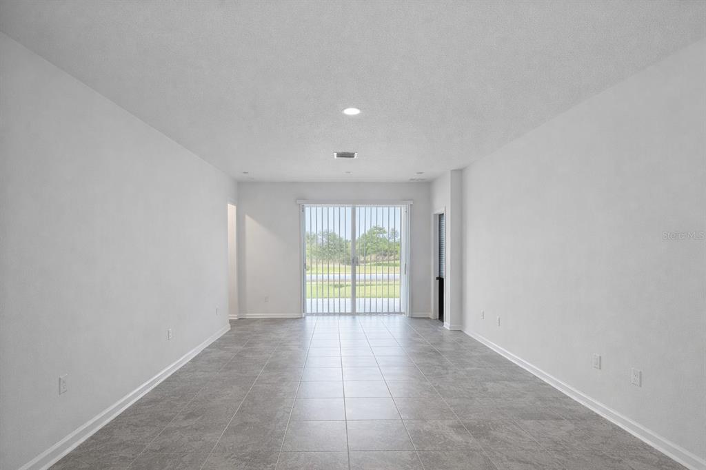 An empty room with gray tile flooring, white walls, and sliding glass doors leading outside — 4086 GOOSEBERRY TRAIL, KISSIMMEE, FL