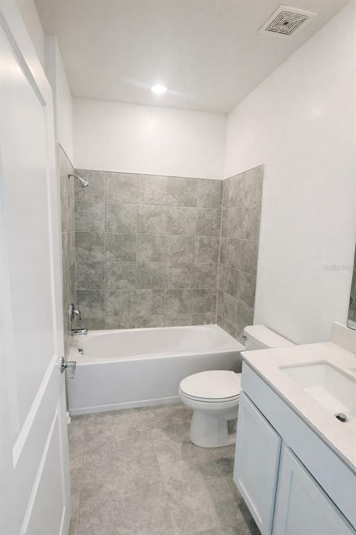 A bathroom features a white vanity, a toilet, and a bathtub with gray tiled walls — 4086 GOOSEBERRY TRAIL, KISSIMMEE, FL