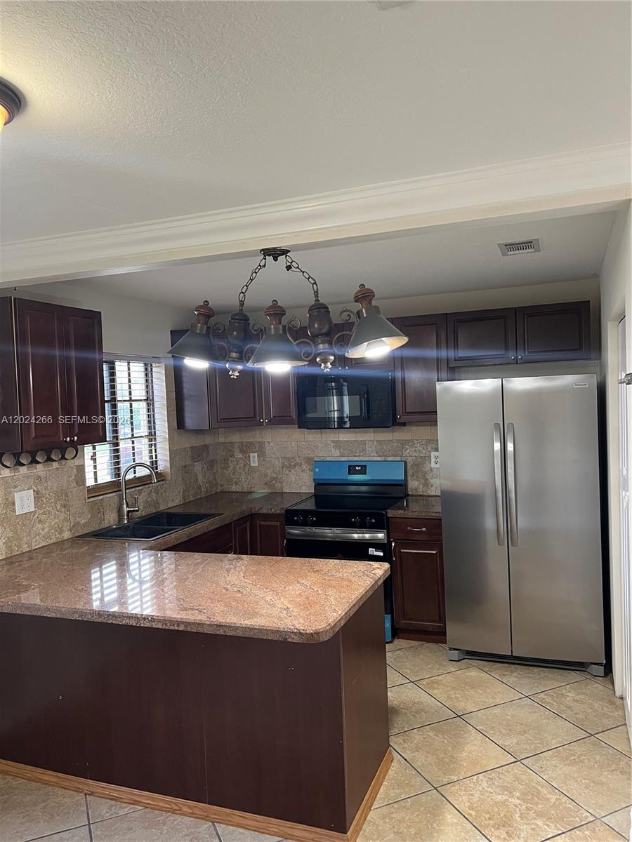 A kitchen features dark wood cabinets, granite countertops, stainless steel appliances, and a hanging chandelier — 1126 NE 209th Ter, Miami FL 33179, MIAMI, FL