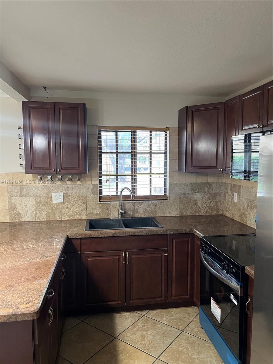 A kitchen features dark wood cabinets, granite countertops, a tiled backsplash, and a double sink — 1126 NE 209th Ter, Miami FL 33179, MIAMI, FL