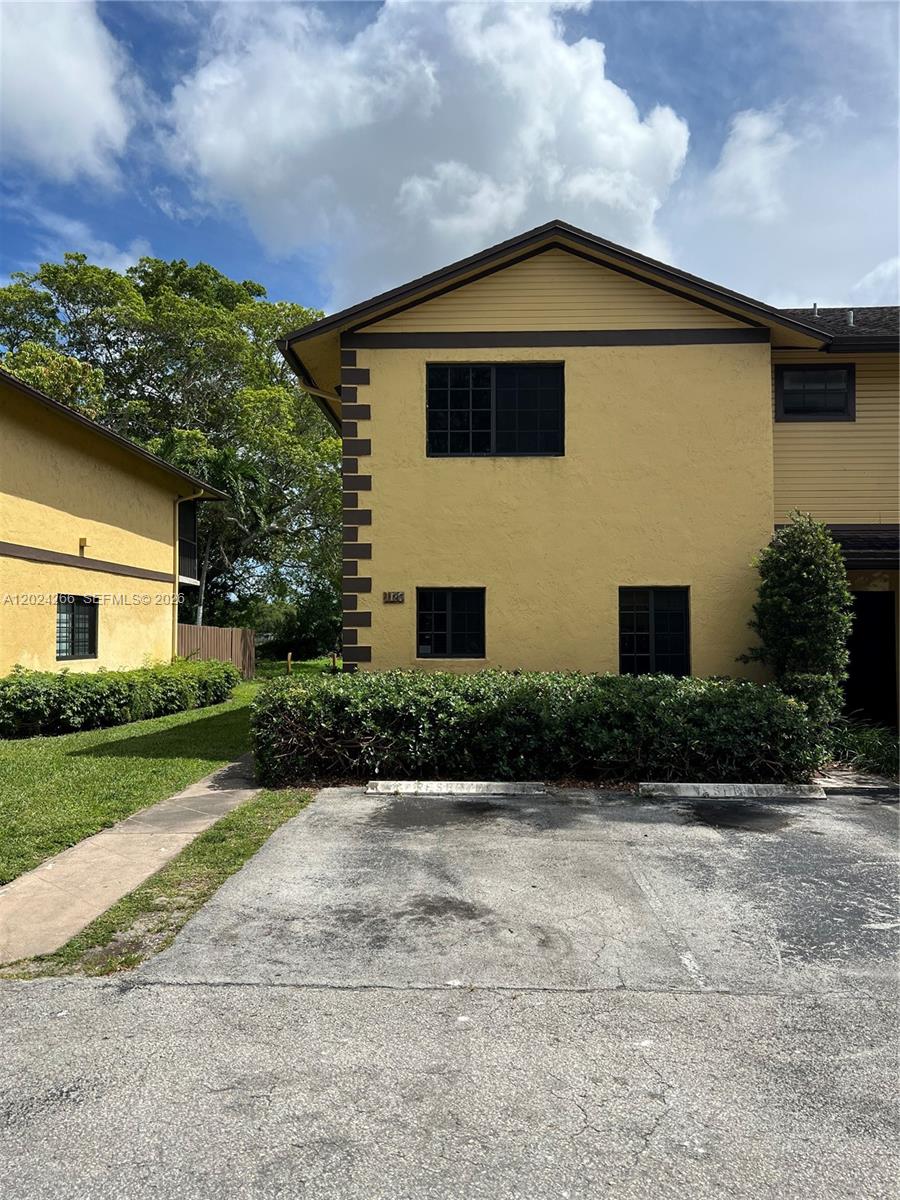 A two-story yellow townhouse with dark trim and a paved parking area in front — 1126 NE 209th Ter, Miami FL 33179, MIAMI, FL