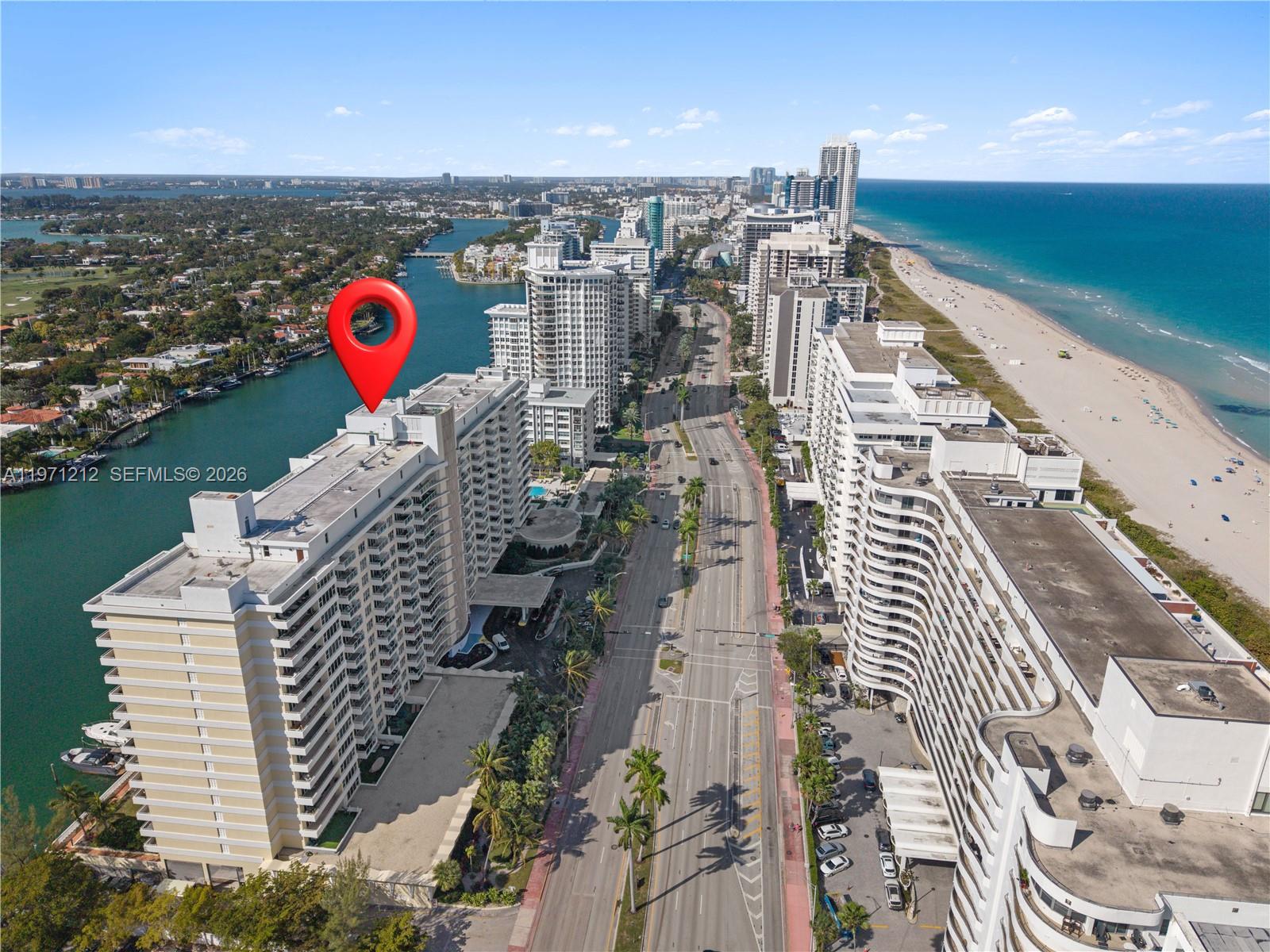 A bedroom features a white bed, a small metal side table, and large windows — 5600 Collins Ave # 16Y, Miami Beach FL 33140, MIAMI BEACH, FL