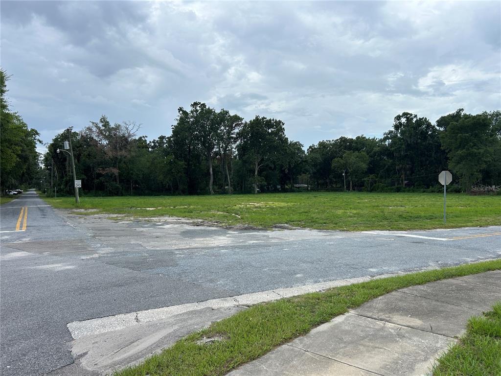 A vacant, grassy corner lot is bordered by paved roads and mature trees — 300 SW 18TH STREET, OCALA, FL