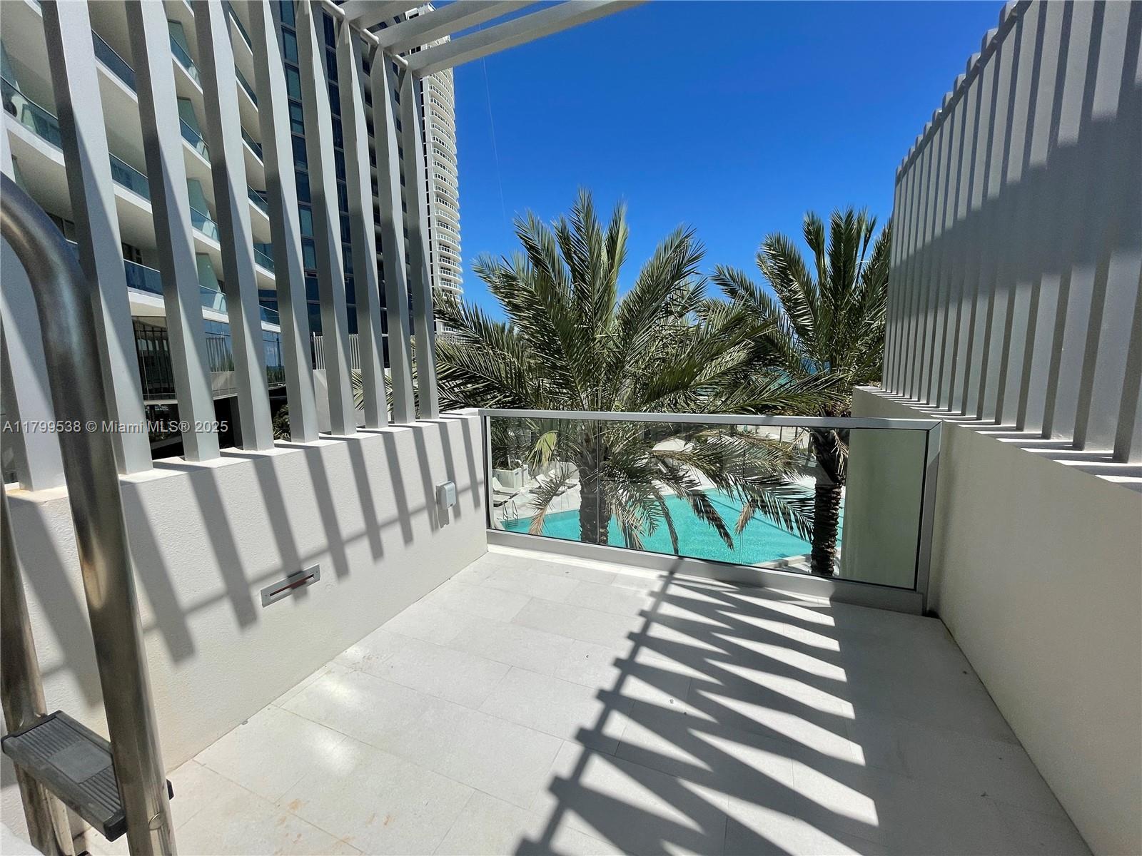 A balcony with a glass railing overlooks a swimming pool and palm trees — 18501 Collins Avenue # 27, Sunny Isles Beach FL 33160, SUNNY ISLES BEACH, FL