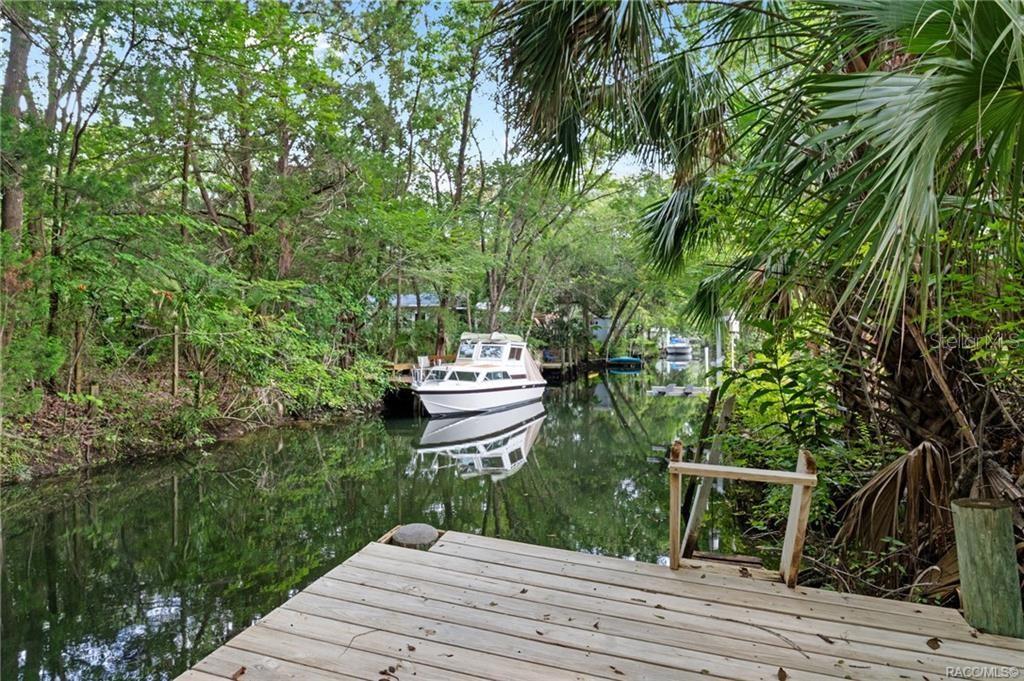 A wooden dock overlooks a narrow canal with a boat moored near lush green trees — 68 CANTERBURY ROAD, INGLIS, FL