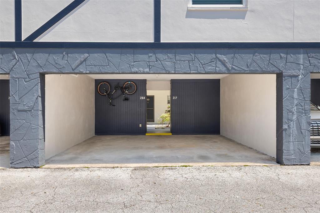 A covered parking area features a dark blue wall with a mounted bicycle — 1147 KING ARTHUR COURT UNIT 204, DUNEDIN, FL