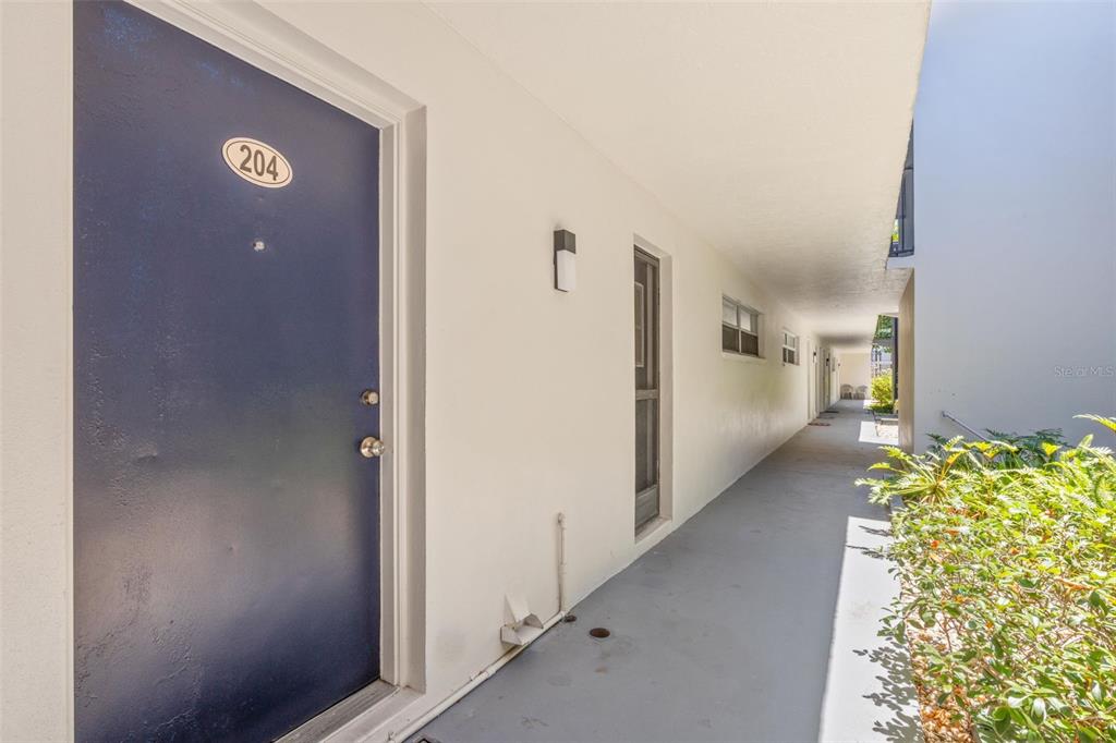 An exterior view of an apartment building walkway with a blue door numbered 204 — 1147 KING ARTHUR COURT UNIT 204, DUNEDIN, FL