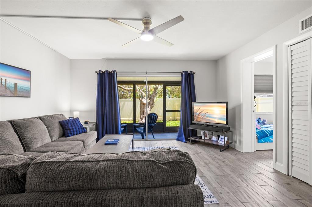 A living room with gray tile floors, a sectional sofa, and sliding doors to a patio — 1147 KING ARTHUR COURT UNIT 204, DUNEDIN, FL