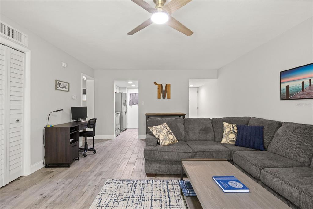 A living room features a gray sectional sofa, a desk, and wood-look tile flooring — 1147 KING ARTHUR COURT UNIT 204, DUNEDIN, FL