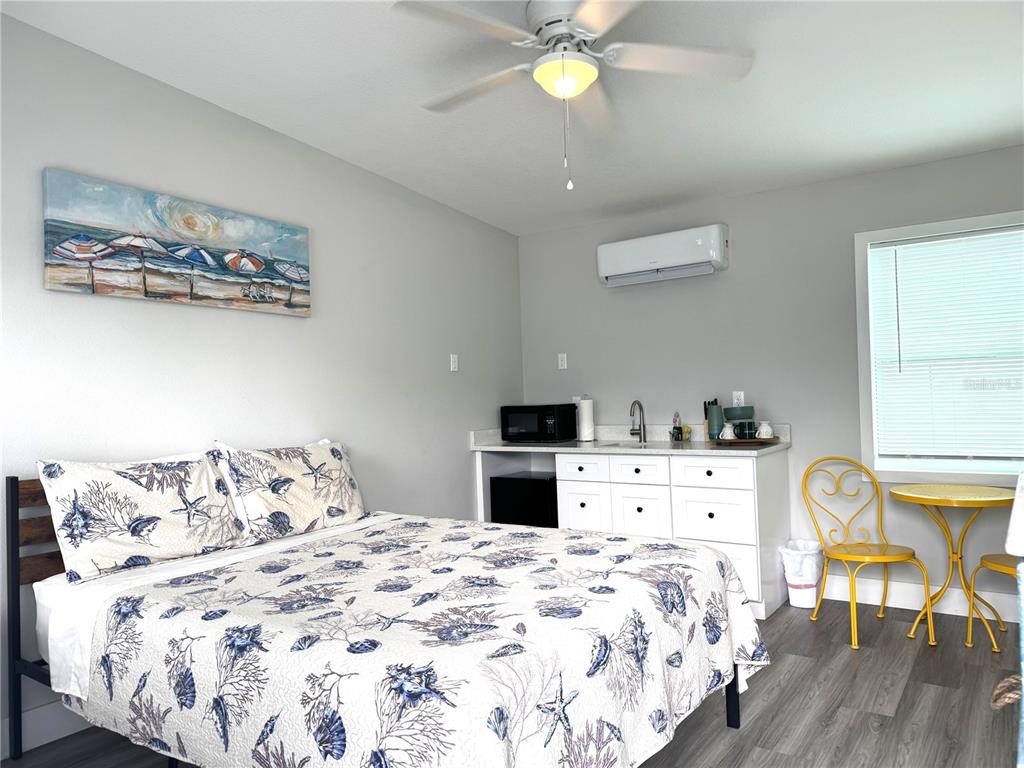 A bedroom features a bed, a small kitchenette with white cabinets, and a yellow bistro set — 13343 GULF BOULEVARD UNIT B5, MADEIRA BEACH, FL