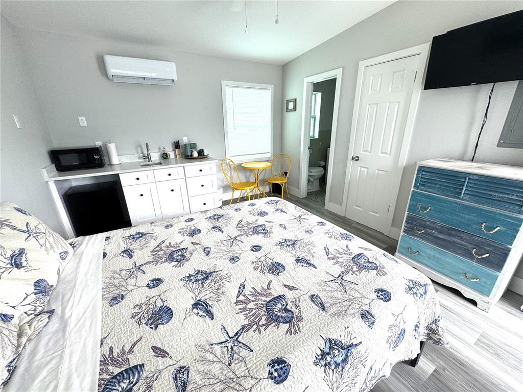 A bedroom features a kitchenette, a bed with a seashell print quilt, and a dresser — 13343 GULF BOULEVARD UNIT B5, MADEIRA BEACH, FL