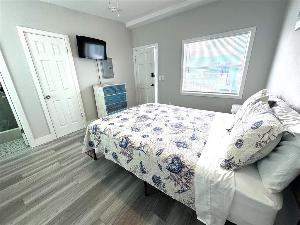A bedroom features a bed with a seashell-patterned quilt, light wood flooring, and two doors — 13343 GULF BOULEVARD UNIT B5, MADEIRA BEACH, FL