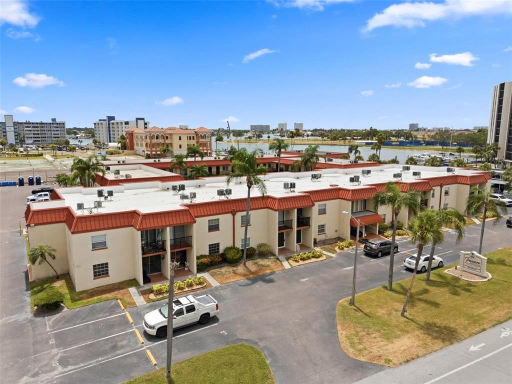 An aerial view shows a multi-story apartment complex with a red roof and parking lot — 10365 PARADISE BOULEVARD UNIT 1, TREASURE ISLAND, FL