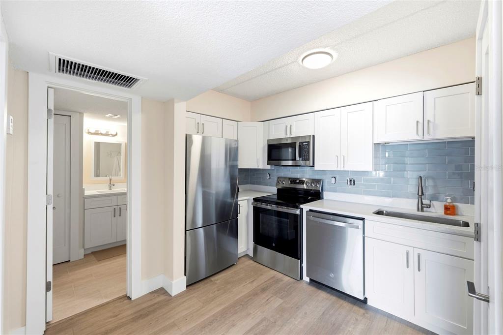 A kitchen with white cabinets, stainless steel appliances, and a light blue subway tile backsplash — 10365 PARADISE BOULEVARD UNIT 1, TREASURE ISLAND, FL