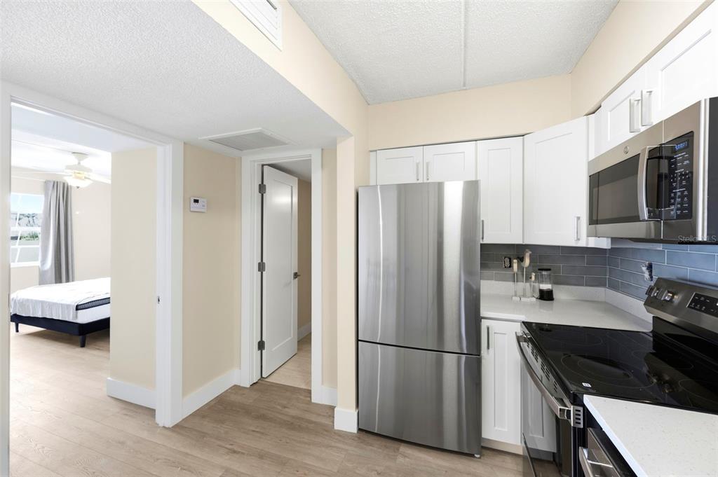 A kitchen with stainless steel appliances, white cabinets, and gray backsplash leads to a bedroom — 10365 PARADISE BOULEVARD UNIT 1, TREASURE ISLAND, FL