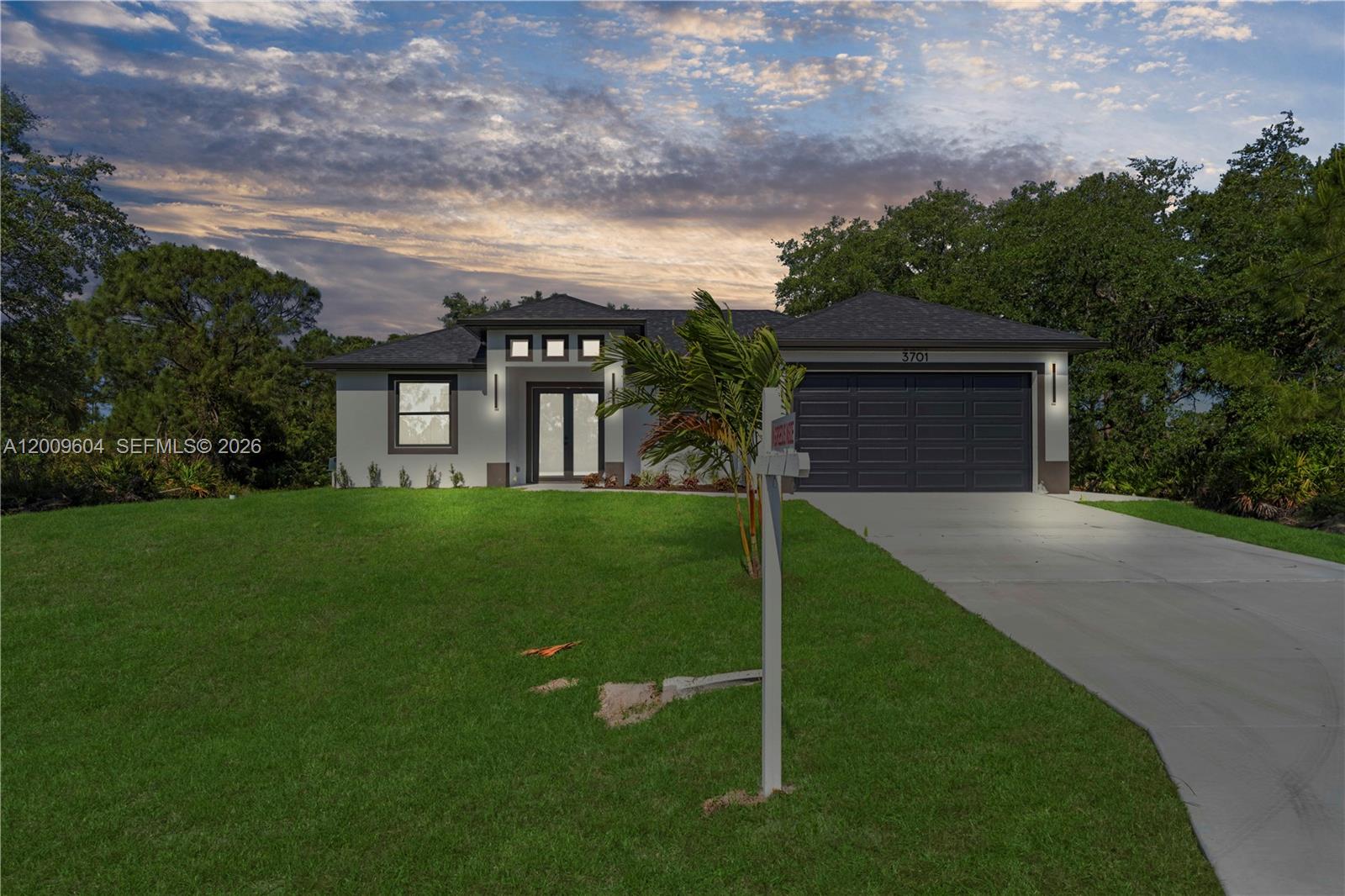 A single-story house with a gray exterior, dark roof, and a concrete driveway at dusk — 3701 Ida Ave N, Lehigh Acres FL 33971, LEHIGH ACRES, FL