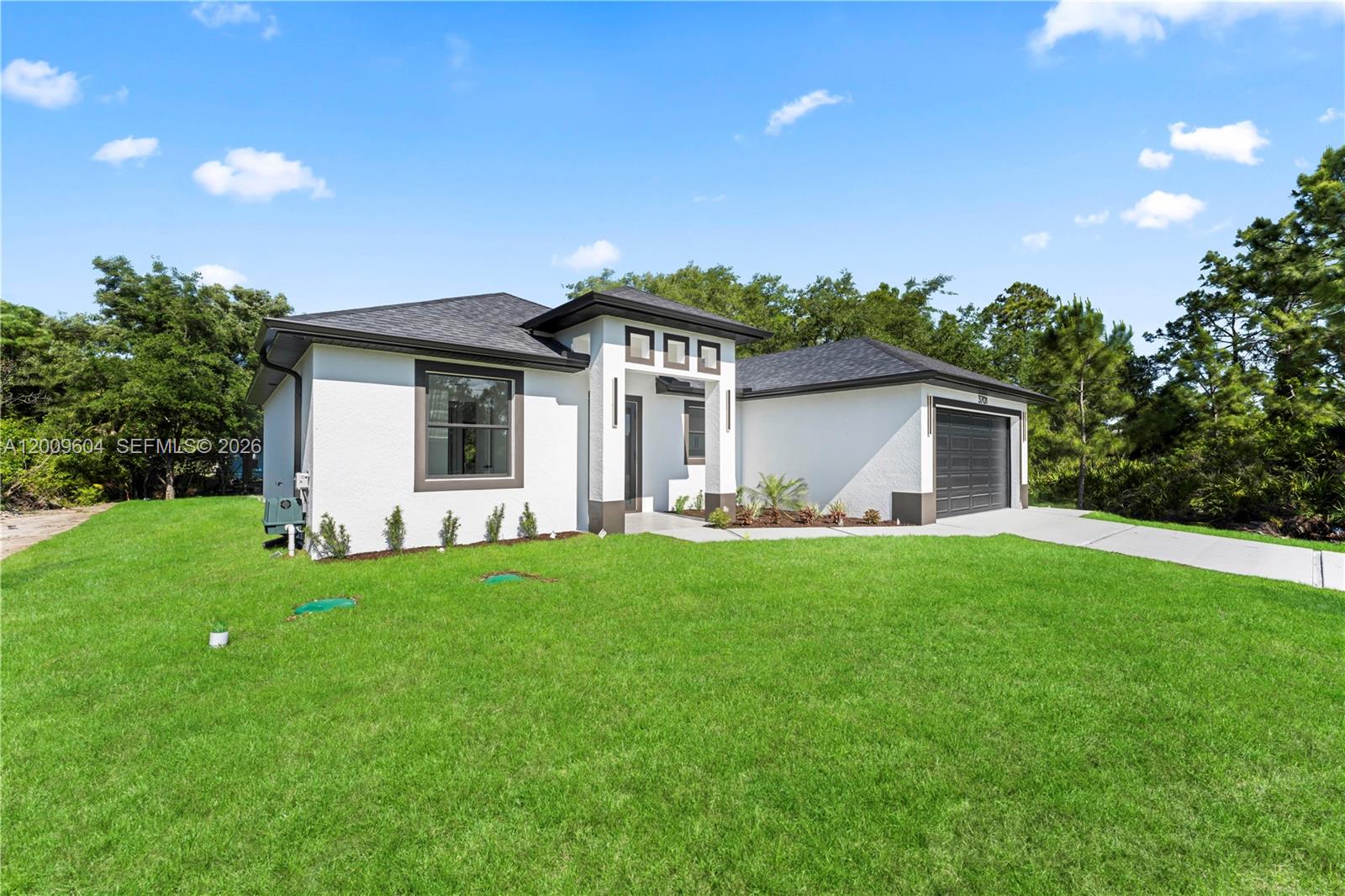 A single-story white house with a dark roof and a two-car garage — 3701 Ida Ave N, Lehigh Acres FL 33971, LEHIGH ACRES, FL