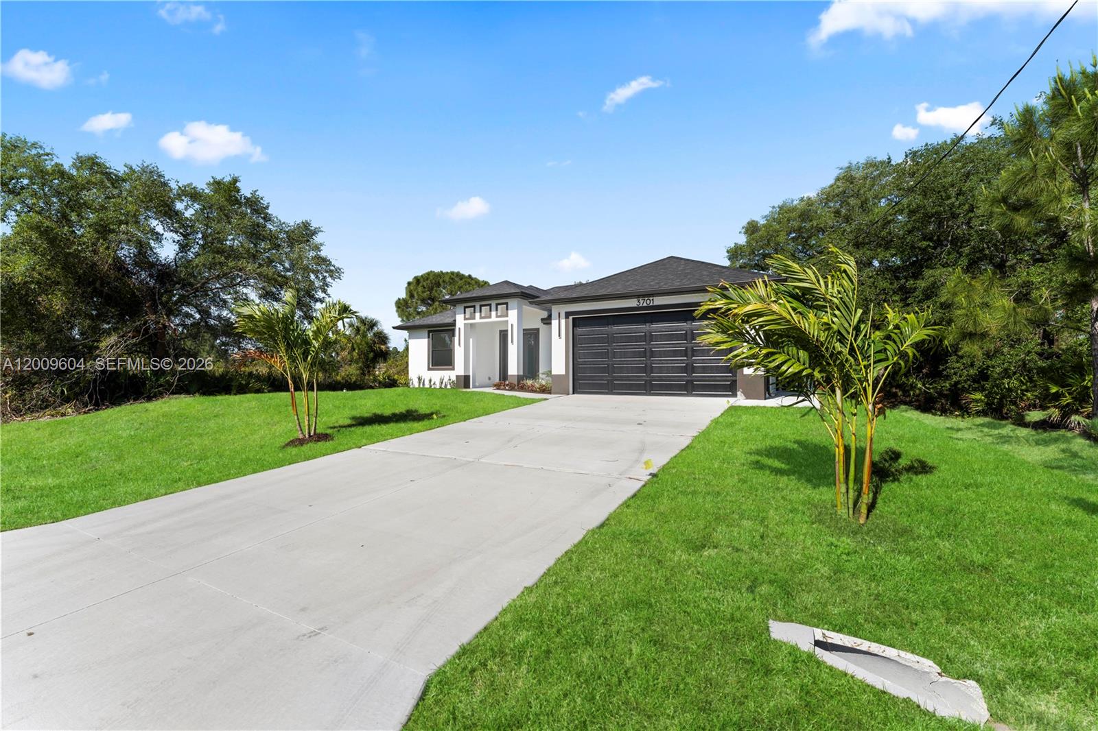 A single-story house with a black garage door and a concrete driveway sits on grass — 3701 Ida Ave N, Lehigh Acres FL 33971, LEHIGH ACRES, FL