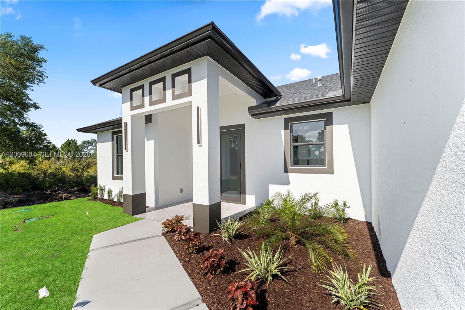 The exterior of a modern white house features a covered entryway with dark trim — 3701 Ida Ave N, Lehigh Acres FL 33971, LEHIGH ACRES, FL