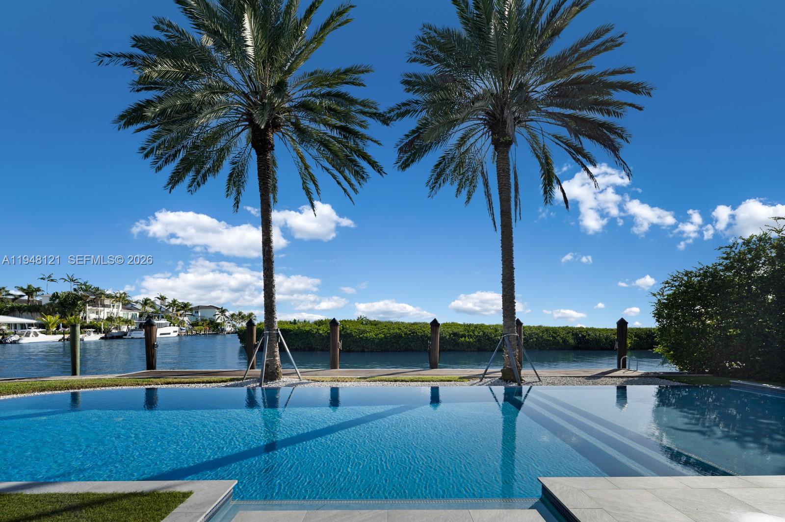 A swimming pool overlooks a canal with two palm trees and a wooden dock — 13009 Mar St, Coral Gables FL 33156, CORAL GABLES, FL