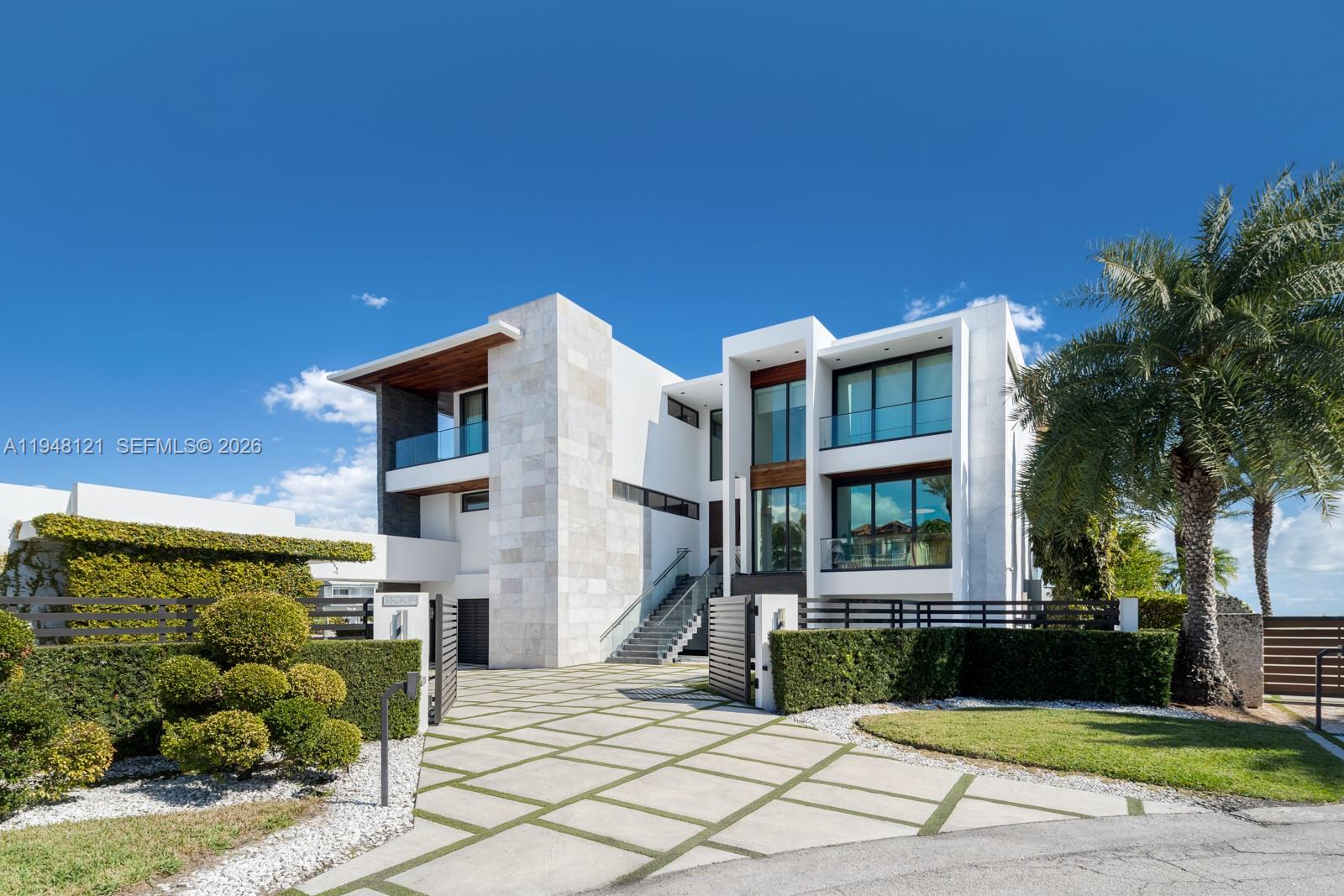 A modern multi-story house features a stone facade, large glass windows, and a paved driveway — 13009 Mar St, Coral Gables FL 33156, CORAL GABLES, FL