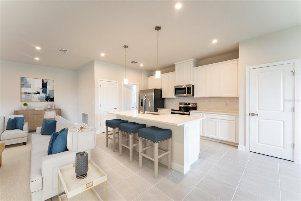 A kitchen with white cabinets and a center island opens into a living room area — 123 VENETIAN PALMS BOULEVARD, NEW SMYRNA BEACH, FL