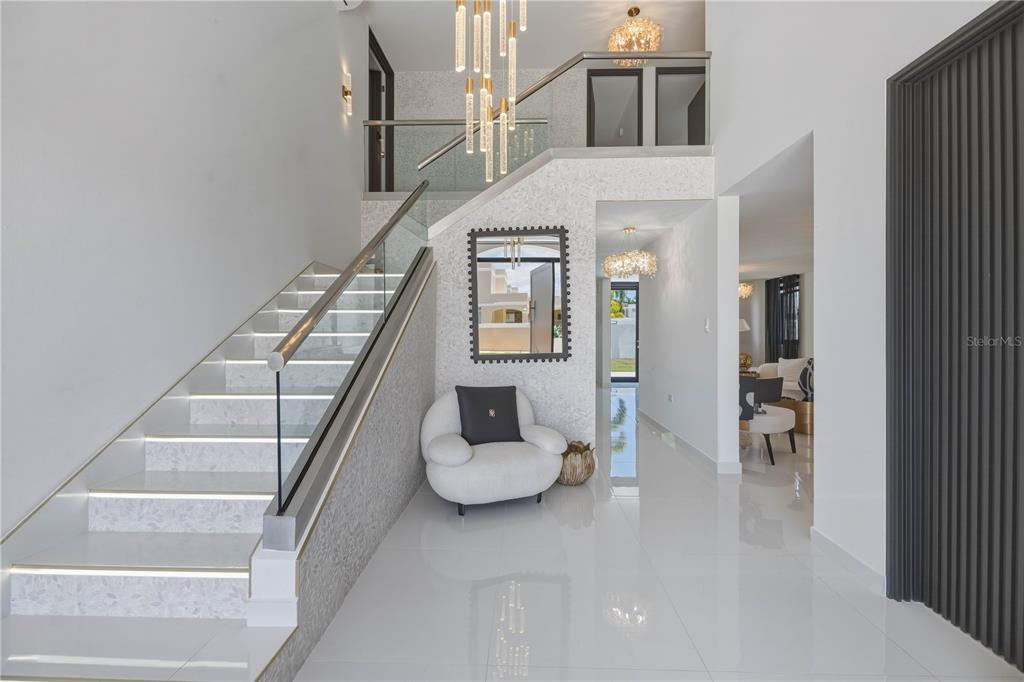 A modern foyer features a glass-railed staircase with illuminated steps and a white armchair — 629 MAR DE BERING, DORADO, PR