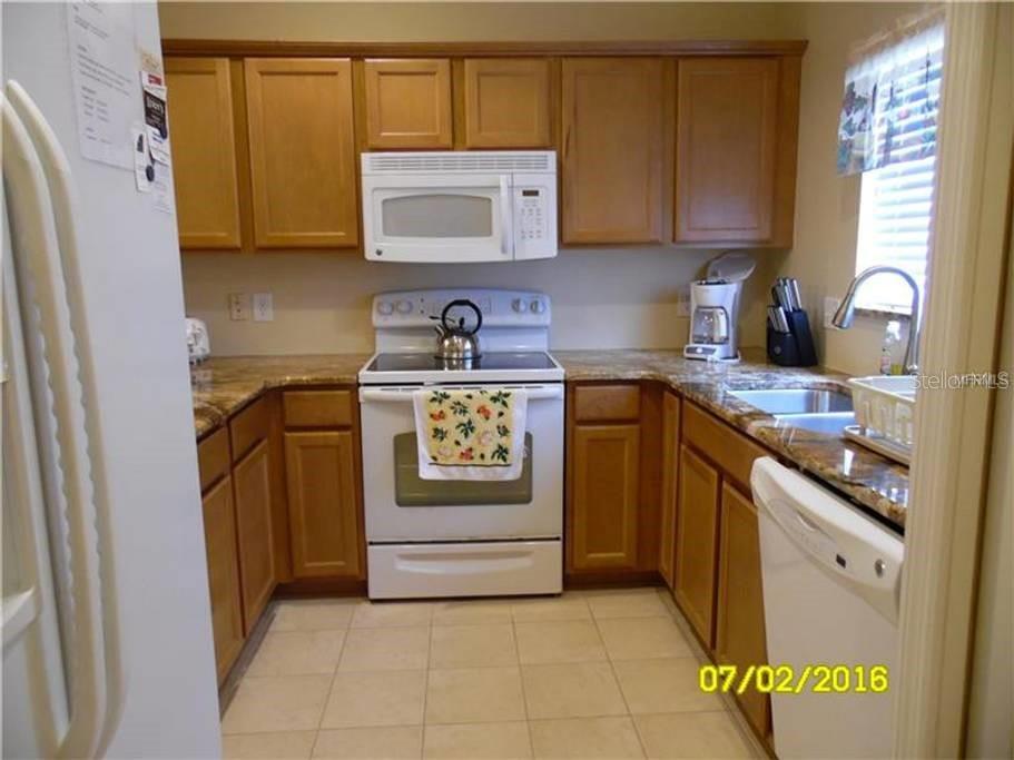 A kitchen features wood cabinets, granite countertops, white appliances, and a tiled floor — 12959 TIGERS EYE DRIVE, VENICE, FL
