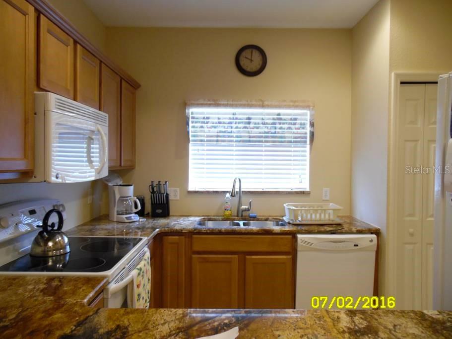 A kitchen features wood cabinets, granite countertops, a stainless steel sink, and white appliances — 12959 TIGERS EYE DRIVE, VENICE, FL
