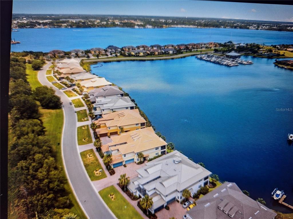An aerial view shows a row of waterfront houses along a curved road and marina — 1121 RIVERSCAPE STREET, BRADENTON, FL