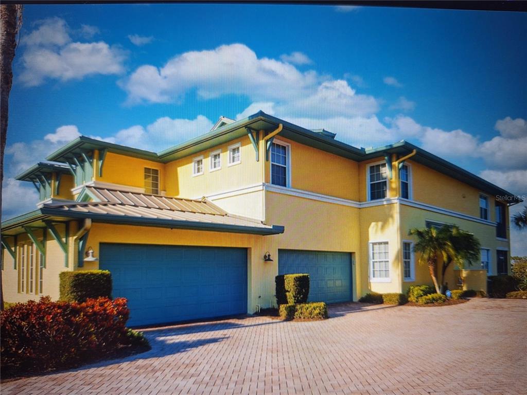 A yellow two-story house with a blue garage and a paved driveway under a blue sky — 1121 RIVERSCAPE STREET, BRADENTON, FL