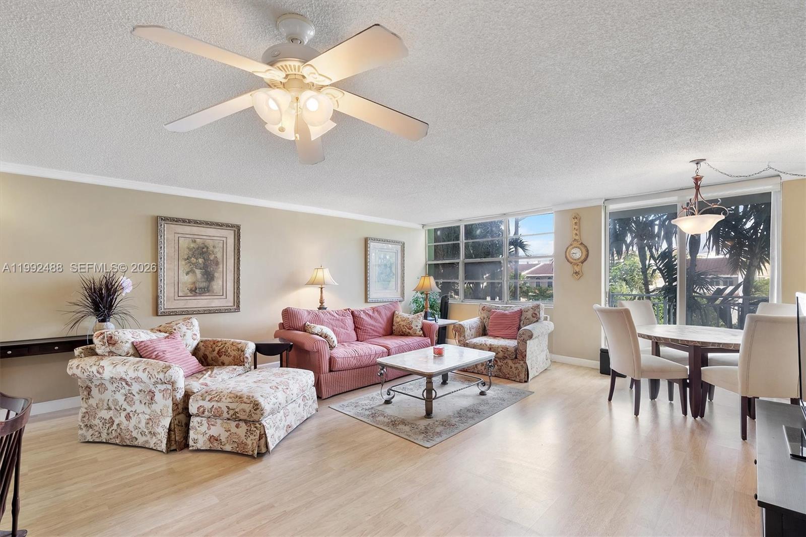 A living and dining room features light wood flooring, floral furniture, and a ceiling fan — 2100 Sans Souci Blvd # B111, North Miami FL 33181, NORTH MIAMI, FL