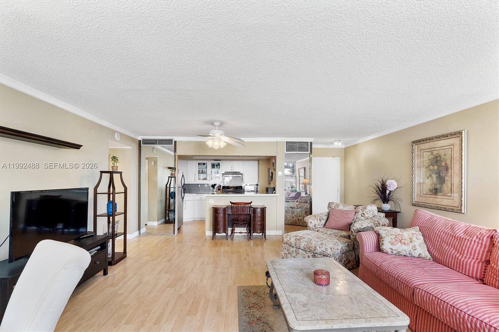 A living room with light wood floors, a striped sofa, and an open kitchen area — 2100 Sans Souci Blvd # B111, North Miami FL 33181, NORTH MIAMI, FL