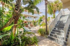 An outdoor courtyard with tropical plants and a staircase leading to a multi-story apartment building — 102 S PENINSULA DRIVE UNIT 201, DAYTONA BEACH, FL