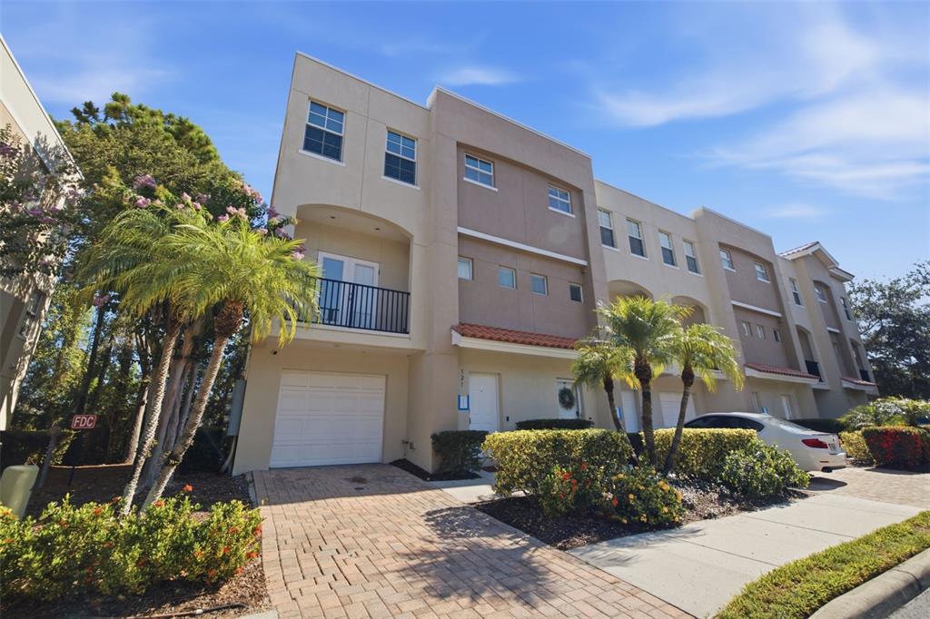A three-story townhouse with a beige stucco exterior, a garage, and a brick driveway — 521 101ST AVENUE N, ST PETERSBURG, FL