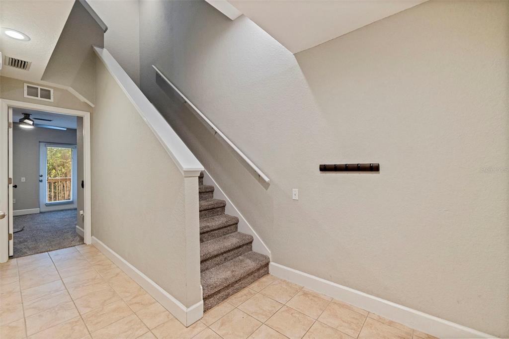 A carpeted staircase with a white railing sits next to a tiled entryway — 521 101ST AVENUE N, ST PETERSBURG, FL