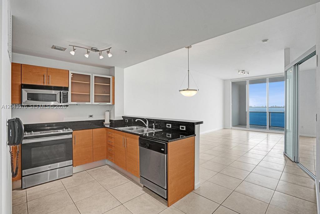 A kitchen with light wood cabinets and black countertops opens to a living area with water views — 725 NE 22nd St # 8B, Miami FL 33137, MIAMI, FL