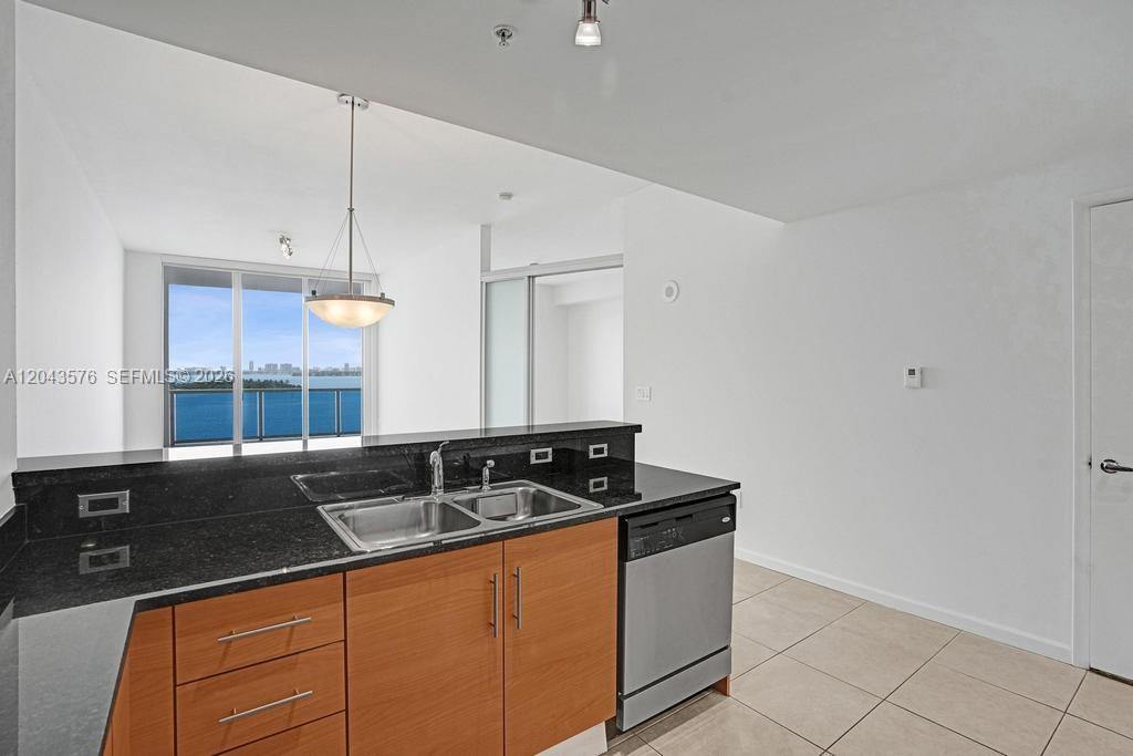 A kitchen with wood cabinets, black countertops, and a stainless steel dishwasher overlooks a balcony — 725 NE 22nd St # 8B, Miami FL 33137, MIAMI, FL