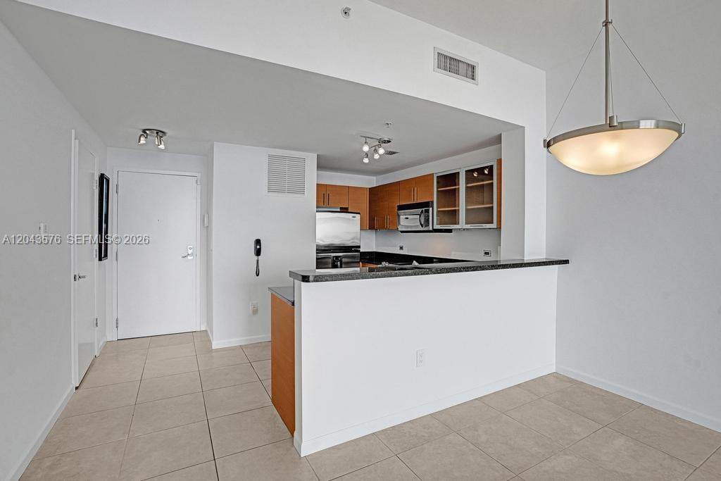 A kitchen with wood cabinets and a breakfast bar overlooks a tiled dining area — 725 NE 22nd St # 8B, Miami FL 33137, MIAMI, FL