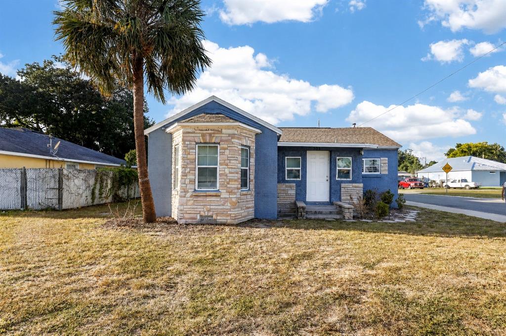 A blue house with a stone-accented bay window and a front door stands on grass — 303 W 5TH STREET, LAKELAND, FL