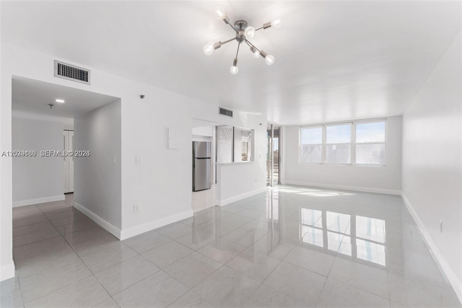 A bright, open-concept living area features white walls, large gray floor tiles, and a modern chandelier — 17890 W Dixie Hwy 501 Hwy # 501, North Miami Beach FL 33160, NORTH MIAMI BEACH, FL