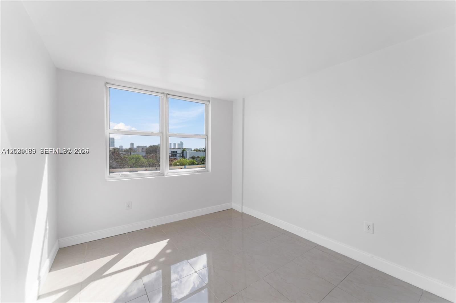 An empty room with white walls, light-colored tile flooring, and a window overlooking a city — 17890 W Dixie Hwy 501 Hwy # 501, North Miami Beach FL 33160, NORTH MIAMI BEACH, FL
