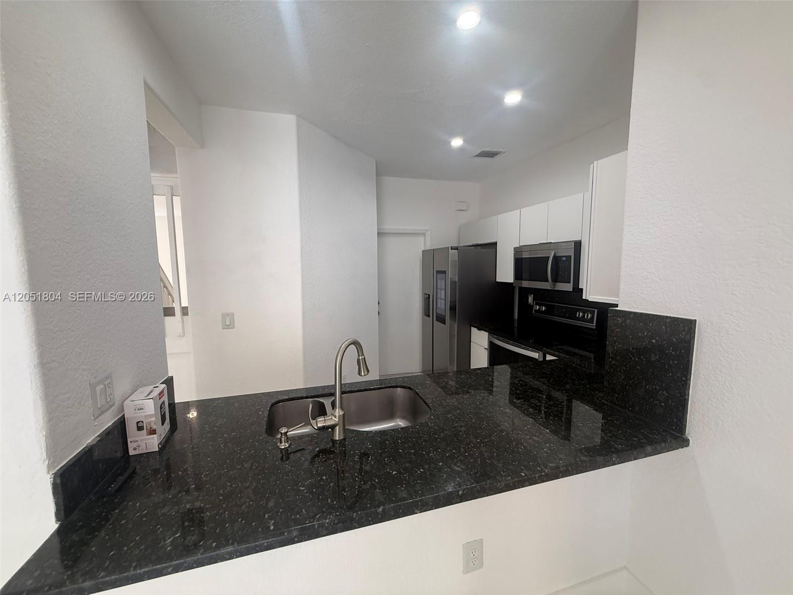 A kitchen features a black granite countertop, stainless steel sink, and white cabinetry — 3873 SW 171st Ter0, Miramar FL 33027, MIRAMAR, FL