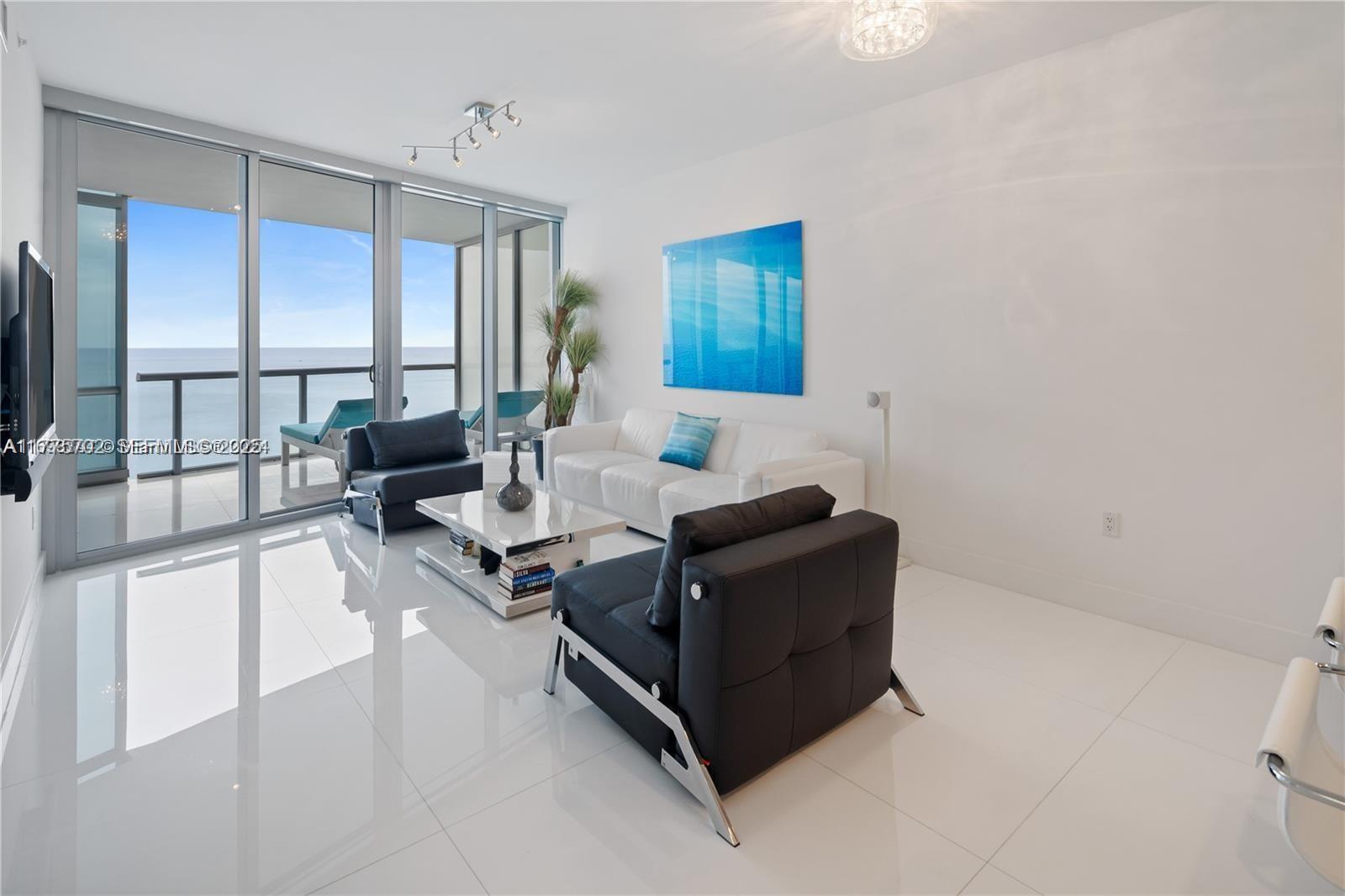 A modern living room features white tile floors, a white sofa, and ocean views — 17121 Collins Ave # 1703, Sunny Isles Beach FL 33160, SUNNY ISLES BEACH, FL
