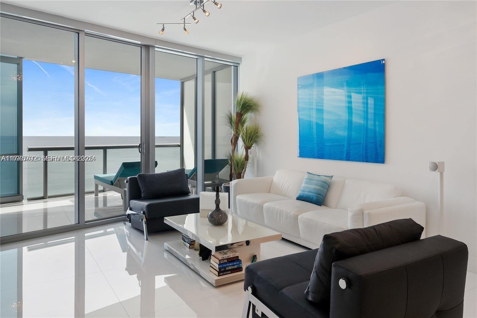 A modern living room features white tile floors, a white sofa, and floor-to-ceiling balcony windows — 17121 Collins Ave # 1703, Sunny Isles Beach FL 33160, SUNNY ISLES BEACH, FL
