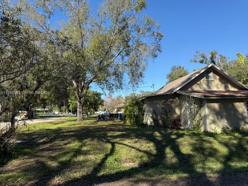 A side view of a tan house with a gabled roof and large trees nearby — 763 ROLFE STREET, Kissimmee FL 34741, KISSIMMEE, FL