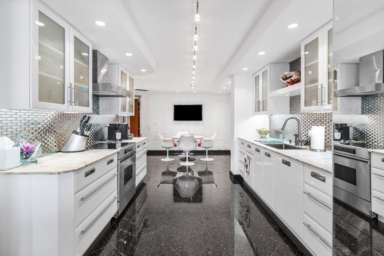 A modern galley kitchen features white cabinetry, stainless steel appliances, and black tiled flooring — 1500 S Ocean Boulevard, Boca Raton FL 33432, BOCA RATON, FL