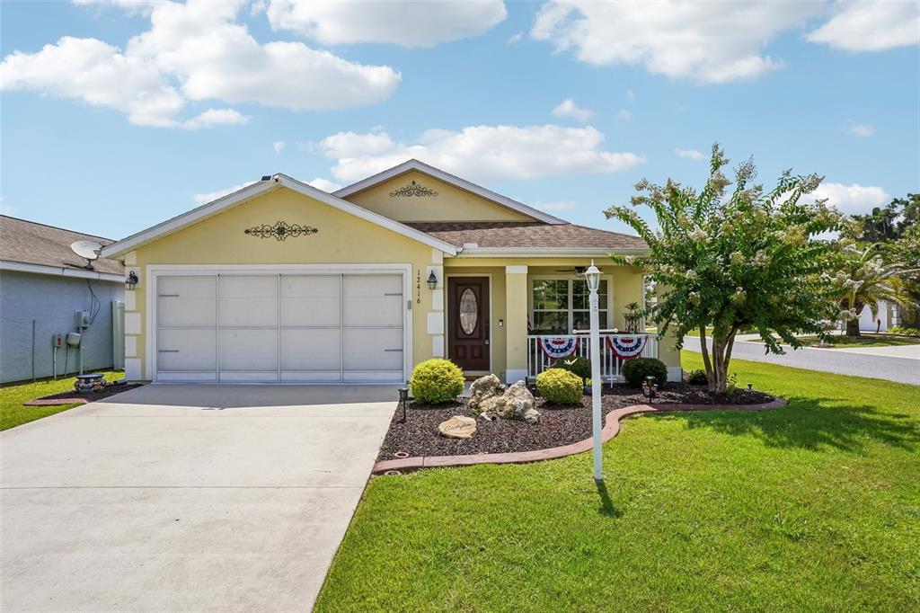 A single-story yellow house features a two-car garage, a front porch, and landscaped yard — 12416 NE 48TH LOOP, OXFORD, FL