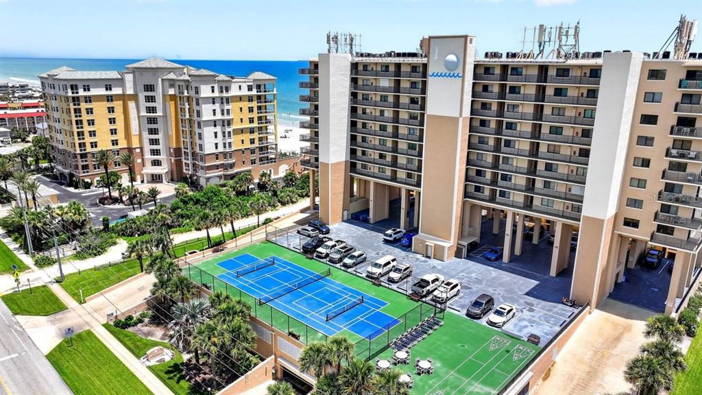 An aerial view shows a multi-story beachfront building with a tennis court and parking lot — 4139 S ATLANTIC AVENUE UNIT B409, NEW SMYRNA BEACH, FL